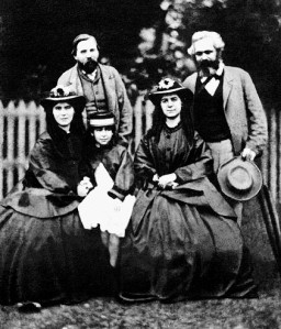 Karl Marx (atrás, derecha) junto con Friedrich Engels (atrás, izquierda), con las hijas de Marx: Jenny Caroline, Jenny Julia Eleanor, y Jenny Laura. Junio de 1864. 